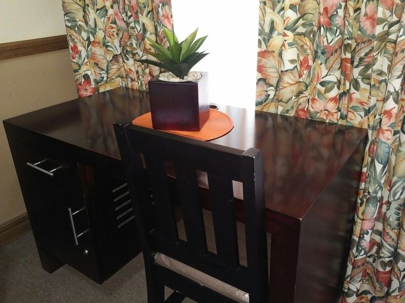 A small office or study area featuring a desk positioned near a window with patterned curtains.