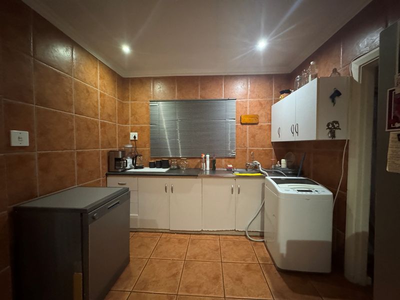 A functional laundry area featuring tiled walls and flooring, built-in cabinetry, and a stainless steel sink with plumbing connections for a washing machine.
