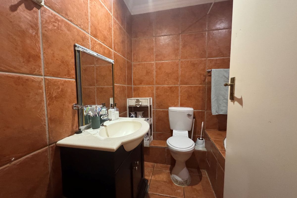 A compact bathroom featuring full-height terracotta-style wall tiling, a vanity cabinet with integrated basin, and a standard toilet.