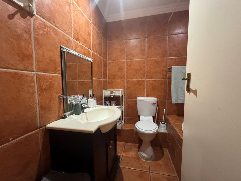 A compact bathroom featuring full-height terracotta-style wall tiling, a vanity cabinet with integrated basin, and a standard toilet.