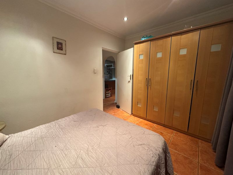 A bedroom featuring built-in wooden wardrobes, tiled flooring, and recessed ceiling lighting, with a view through to an adjacent room.