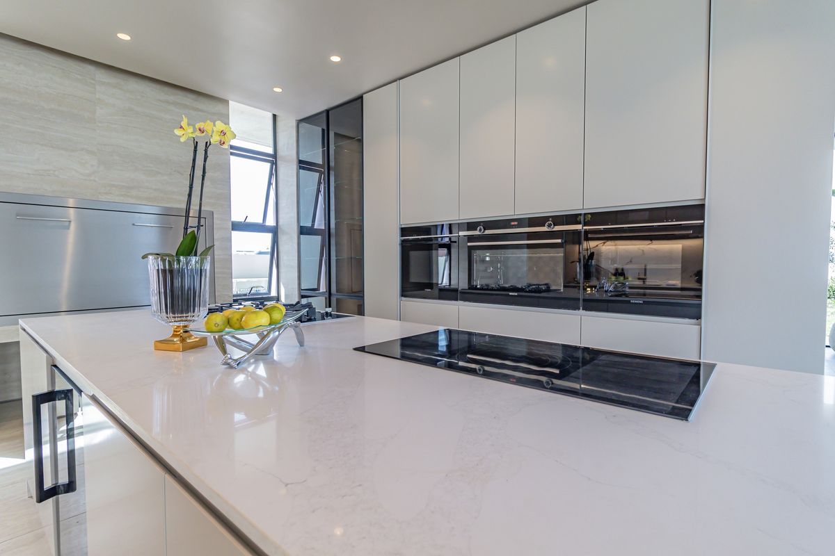 Modern kitchen featuring a large stone-topped island with an integrated induction cooktop, sleek handleless cabinetry, and built-in high-end appliances.