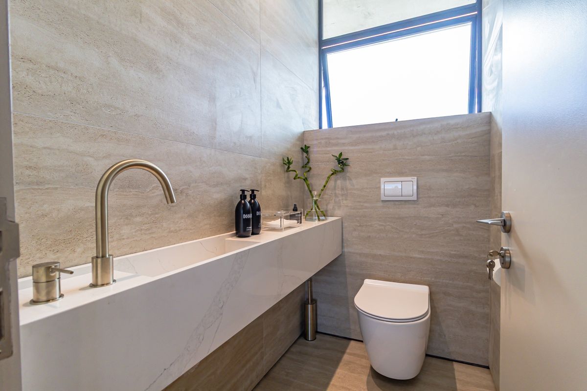 Modern powder room featuring a sleek wall-mounted stone vanity, contemporary brass faucet, and a wall-hung toilet with integrated flush plate.