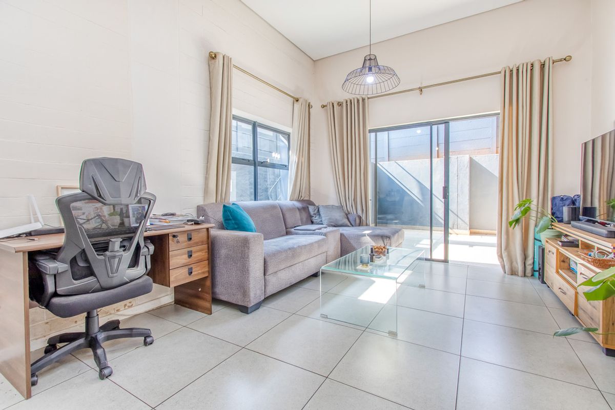 A bright living room featuring large format floor tiles, high ceilings, and sliding glass doors providing direct access to an outdoor patio area.