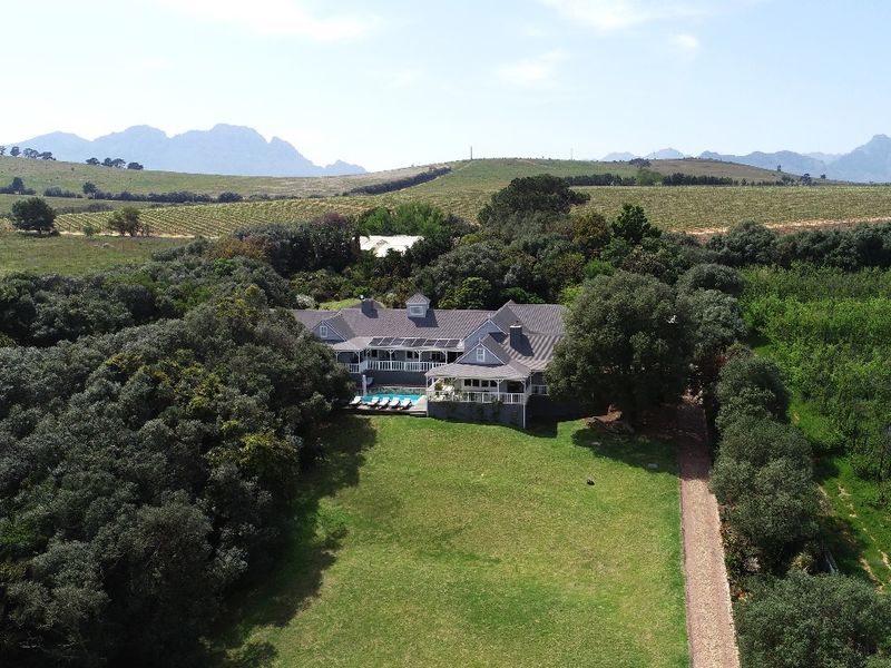 Aerial view of a large rural property featuring a main residence with a swimming pool, solar panels, and expansive surrounding grounds.