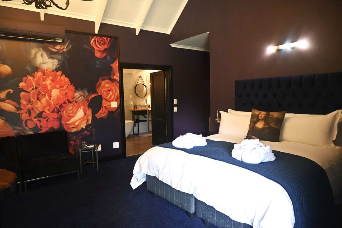 A well-appointed bedroom featuring a vaulted ceiling, dark feature wall with floral wallpaper, and direct access to an en-suite bathroom.