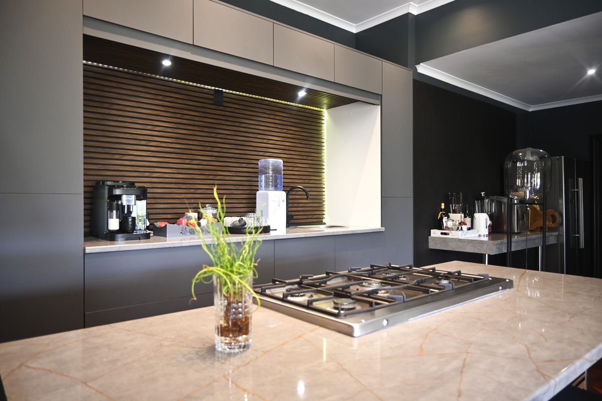 Modern kitchen featuring dark matte cabinetry, a stone-topped island with an integrated gas hob, and a stylish slatted timber feature wall with recessed lighting.