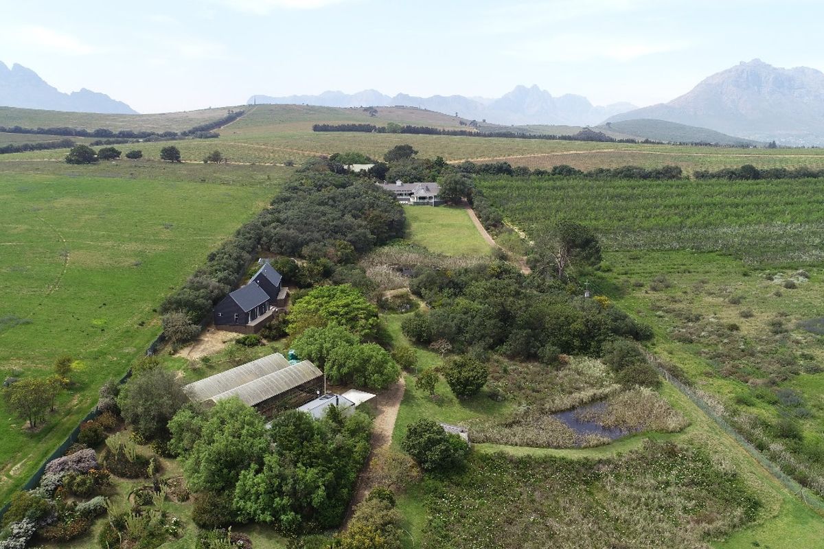 Aerial view of the small holding property featuring multiple structures, a greenhouse, a pond, and expansive surrounding agricultural land with mountain views.
