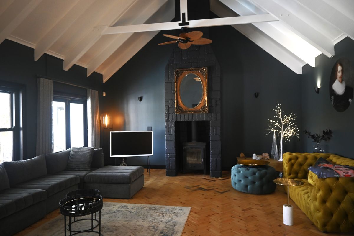 Spacious living room featuring a dramatic vaulted ceiling with exposed trusses, dark feature walls, a central fireplace, and elegant herringbone parquet flooring.