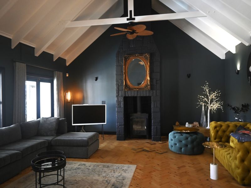 Spacious living room featuring a dramatic vaulted ceiling with exposed trusses, dark feature walls, a central fireplace, and elegant herringbone parquet flooring.