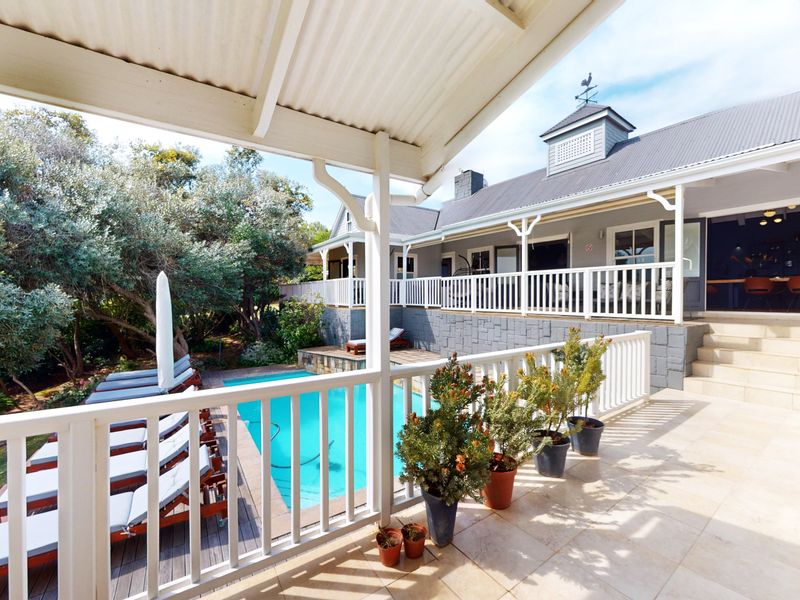 Spacious covered patio overlooking a swimming pool, featuring stone tiling, timber decking, and white railings, ideal for outdoor entertainment.
