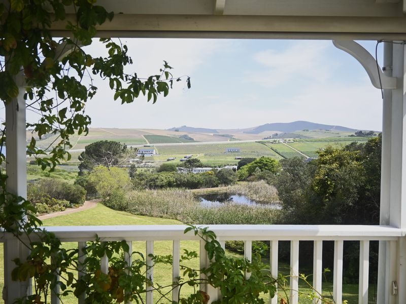 A scenic view overlooking a lush green landscape, pond, and rolling hills, framed by a white timber patio balustrade.