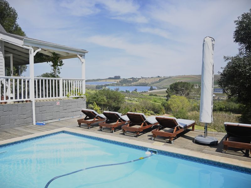 Outdoor pool area featuring timber decking, a covered patio with white railings, and scenic views of the surrounding landscape.
