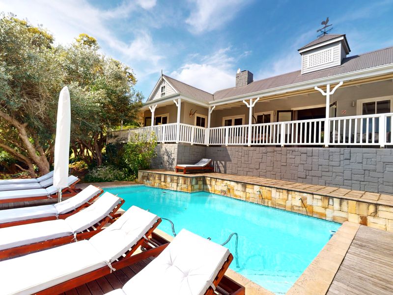 A well-maintained pool area featuring a swimming pool with stone-clad retaining walls, timber decking, and a spacious covered veranda with white railings.