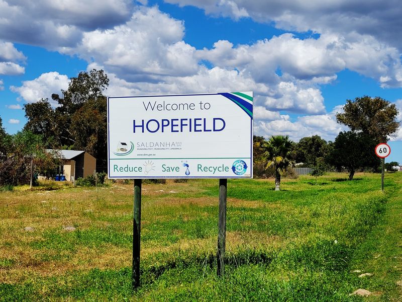 A roadside welcome sign for the town of Hopefield, situated in a rural landscape setting.