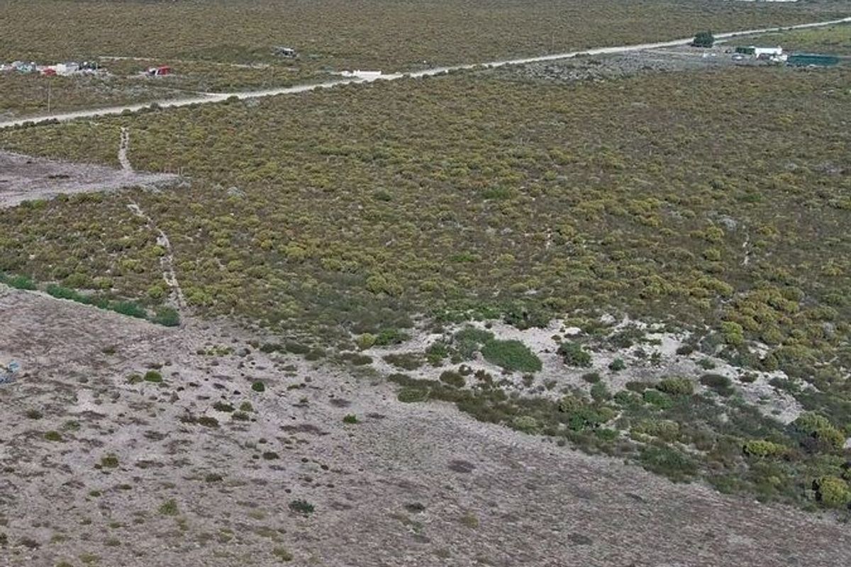 An aerial view of a large, undeveloped small holding plot featuring natural vegetation and a gravel access road.