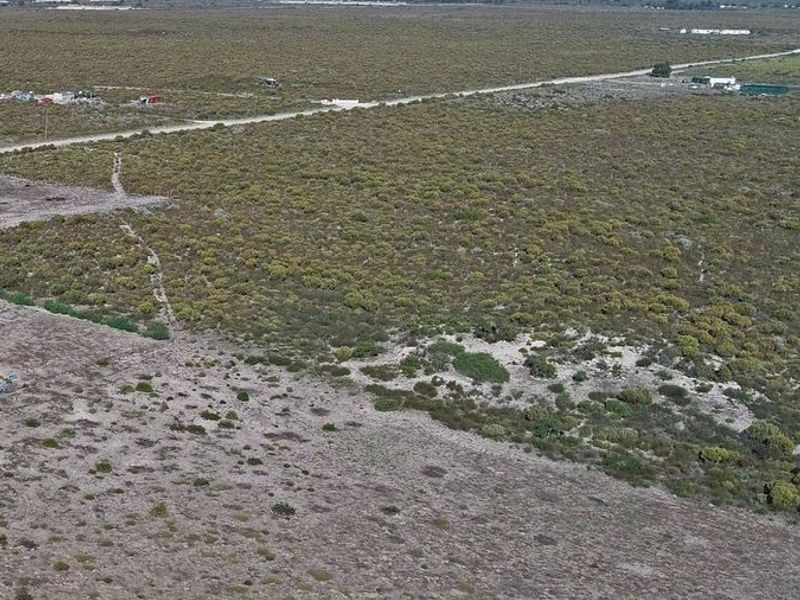 An aerial view of a large, undeveloped small holding plot featuring natural vegetation and a gravel access road.