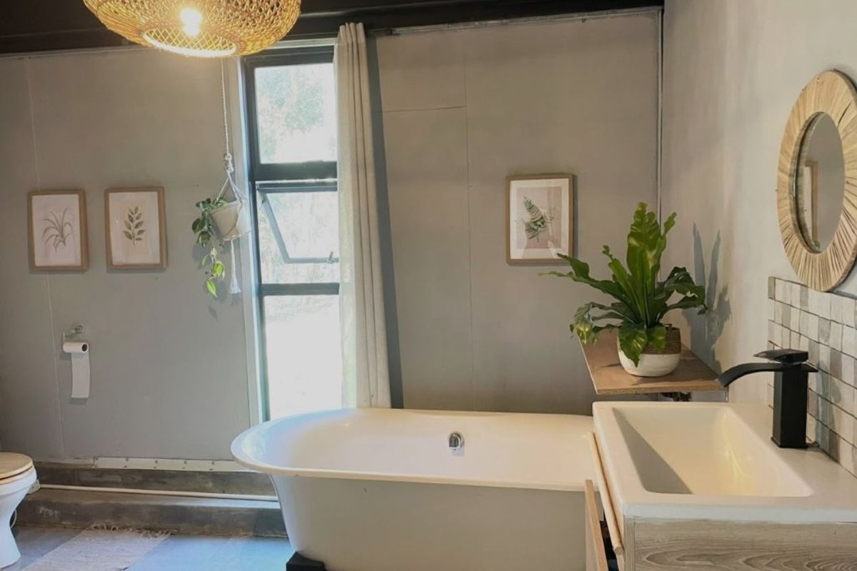 A bathroom featuring a freestanding bathtub, modern vanity basin with black fixtures, and large window, showcasing a contemporary aesthetic with some unfinished wall details.