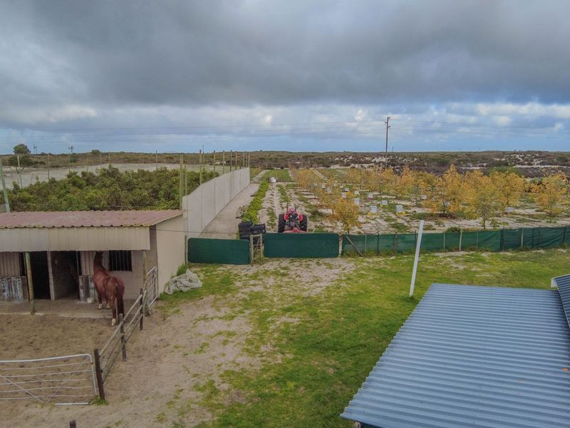 Aerial view of a small holding featuring stables, an orchard, and fenced agricultural land under a cloudy sky.