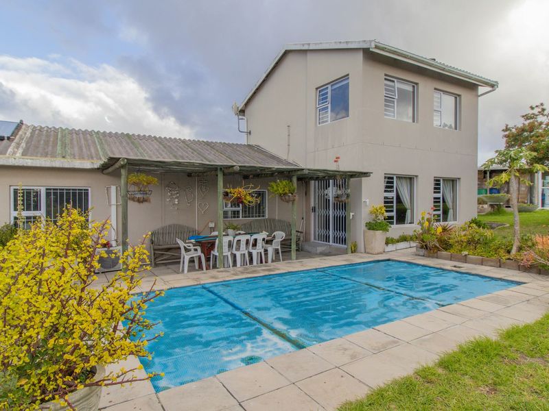 Rear exterior view of the property featuring a swimming pool, paved deck area, and a covered patio attached to the main dwelling.