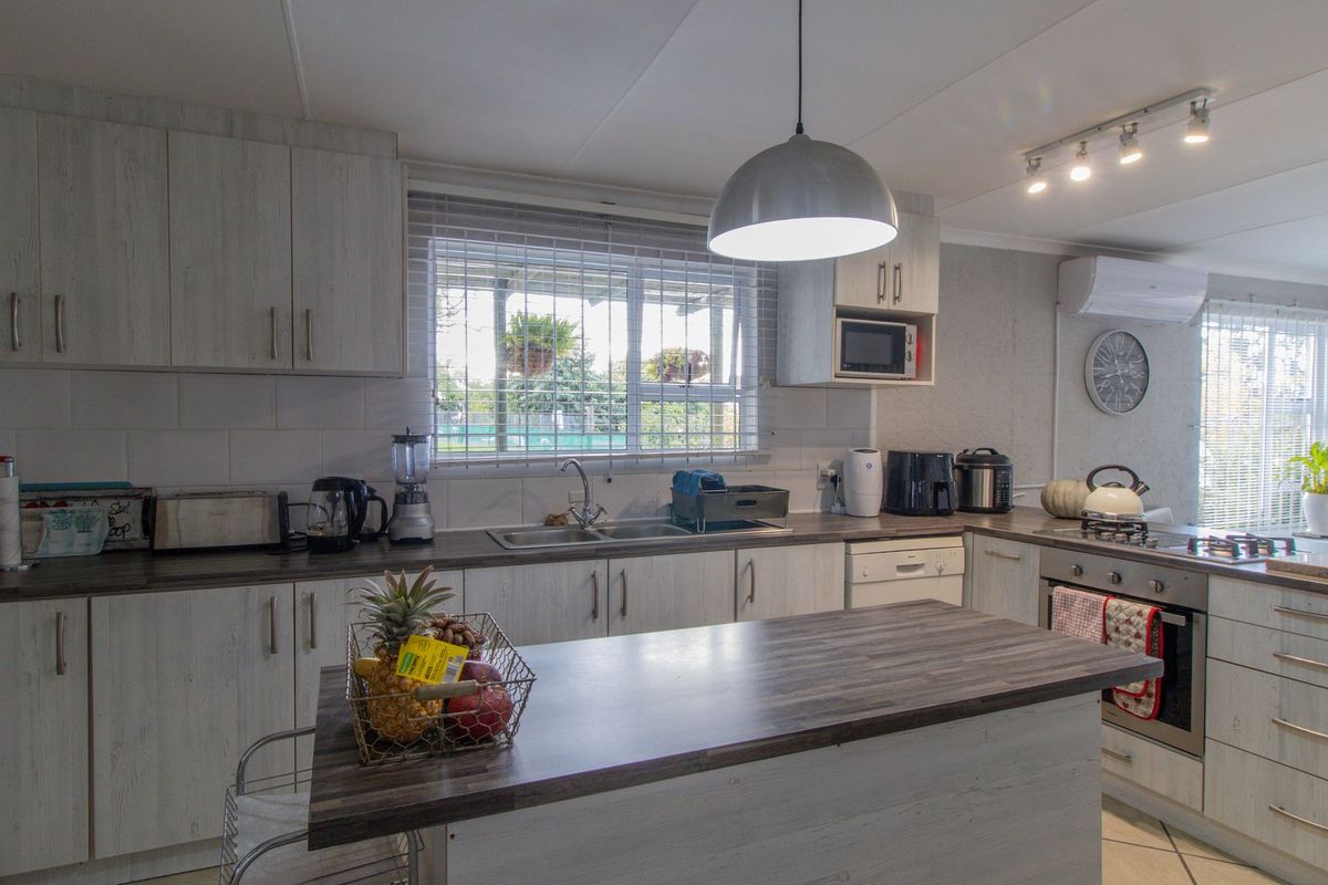A well-maintained kitchen featuring light wood-grain cabinetry, dark laminate countertops, a central island, and integrated appliances including an oven and hob.