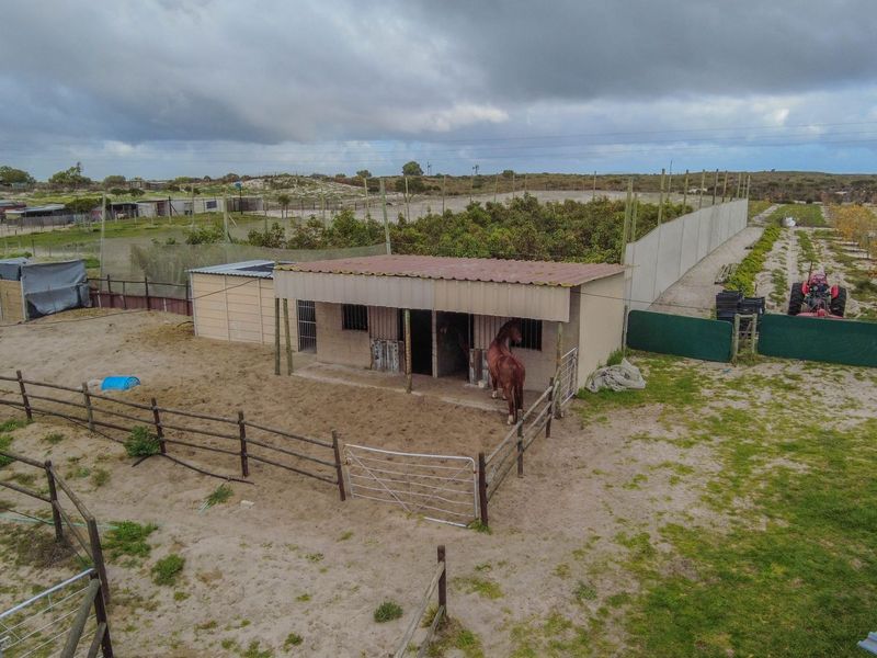 Aerial view of a small holding property featuring stables, fenced paddocks, and agricultural land with a concrete boundary wall.