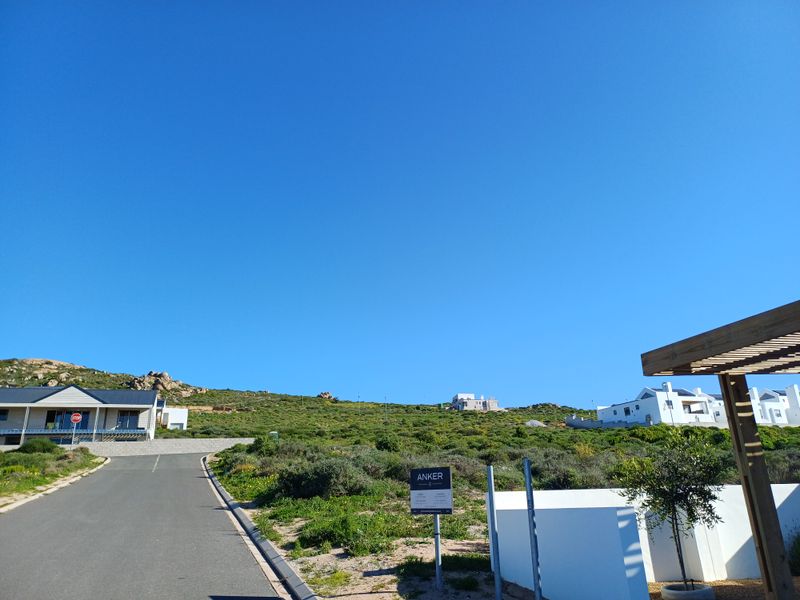 A view of the street and surrounding landscape in a residential estate, featuring paved roads and nearby modern coastal homes.