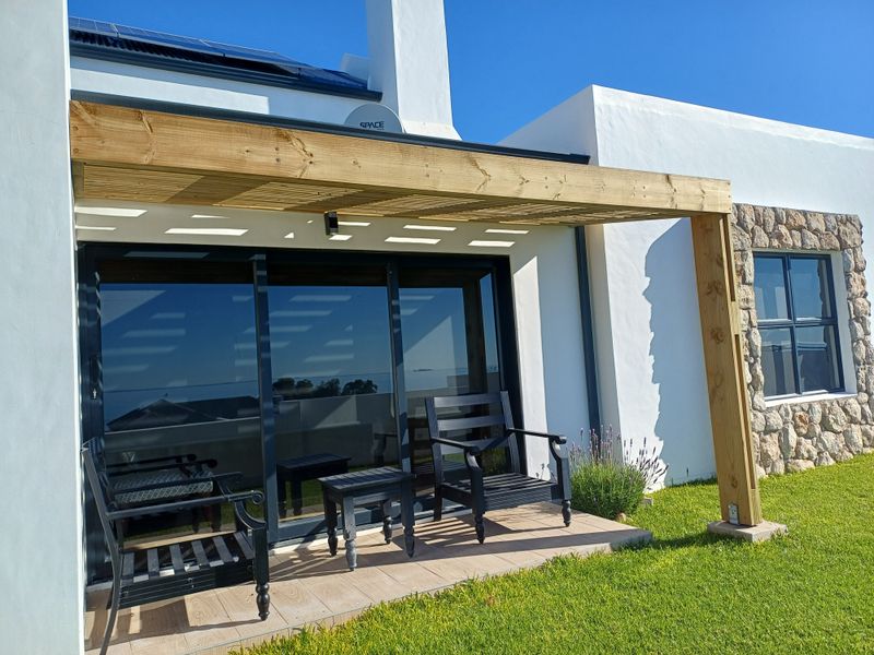 A well-maintained patio area featuring a timber pergola, sliding glass doors, and stone-clad exterior wall, set against a neat garden.