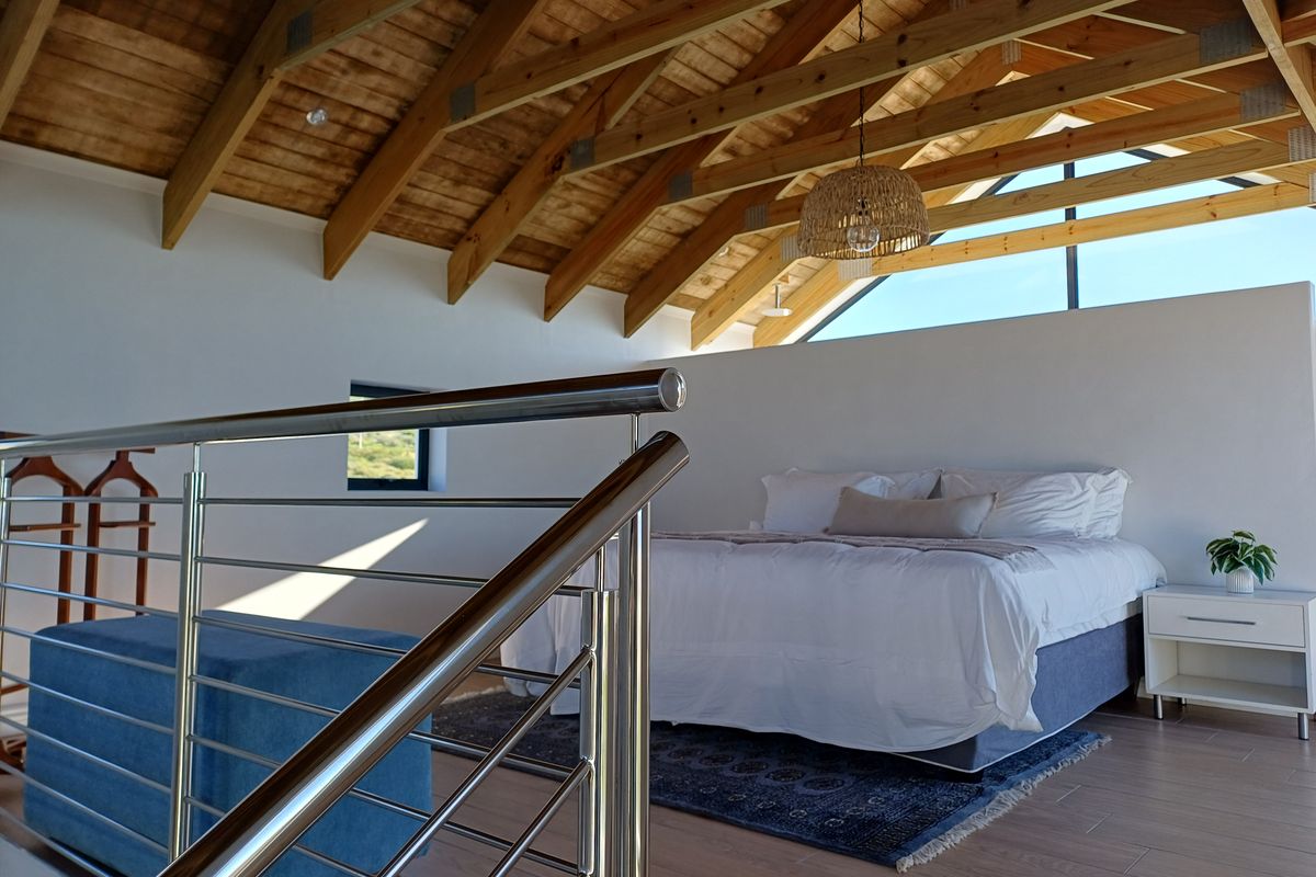 Spacious bedroom featuring high vaulted ceilings with exposed timber trusses, modern stainless steel balustrade, and large triangular clerestory windows providing natural light.
