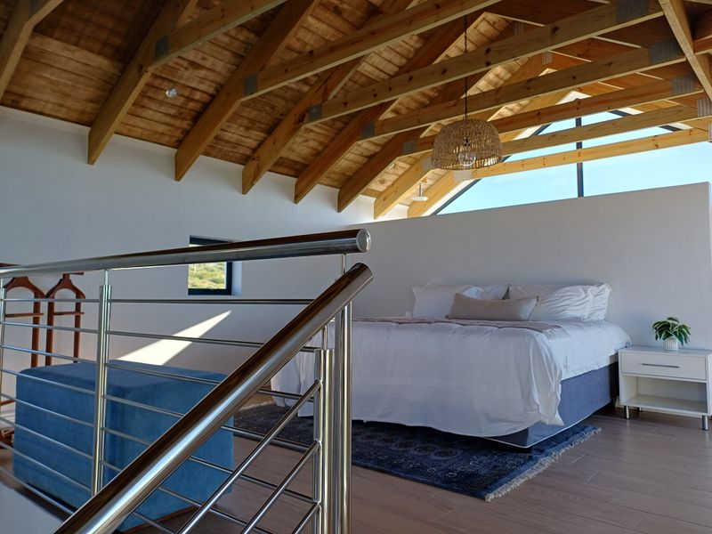 Spacious bedroom featuring high vaulted ceilings with exposed timber trusses, modern stainless steel balustrade, and large triangular clerestory windows providing natural light.