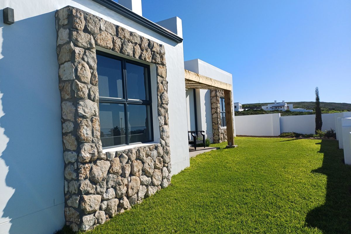 Rear view of the property featuring stone-clad window surrounds, a timber pergola, and a well-maintained lawn enclosed by a boundary wall.