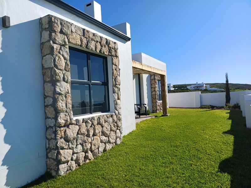 Rear view of the property featuring stone-clad window surrounds, a timber pergola, and a well-maintained lawn enclosed by a boundary wall.