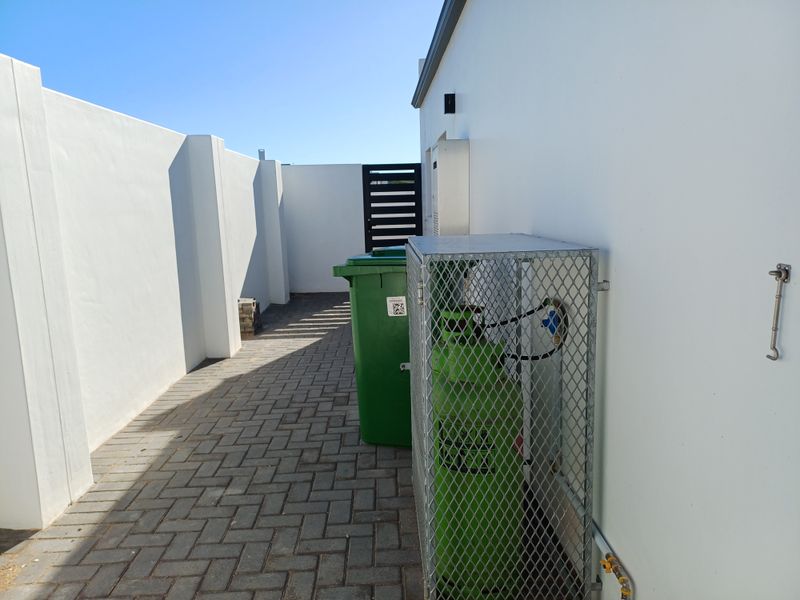 A clean side utility area featuring paved flooring, a secure gas cylinder cage, and high boundary walls.