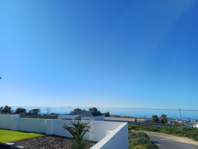A clear, elevated view of the coastline and ocean, featuring a modern white boundary wall in the foreground.