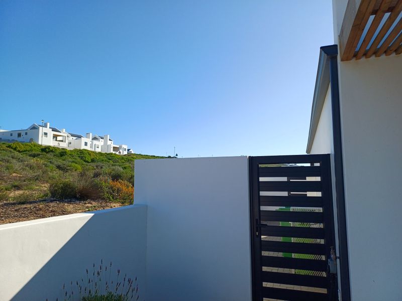 A view of the rear exterior area featuring a modern boundary wall, a secure metal gate, and a timber pergola structure.