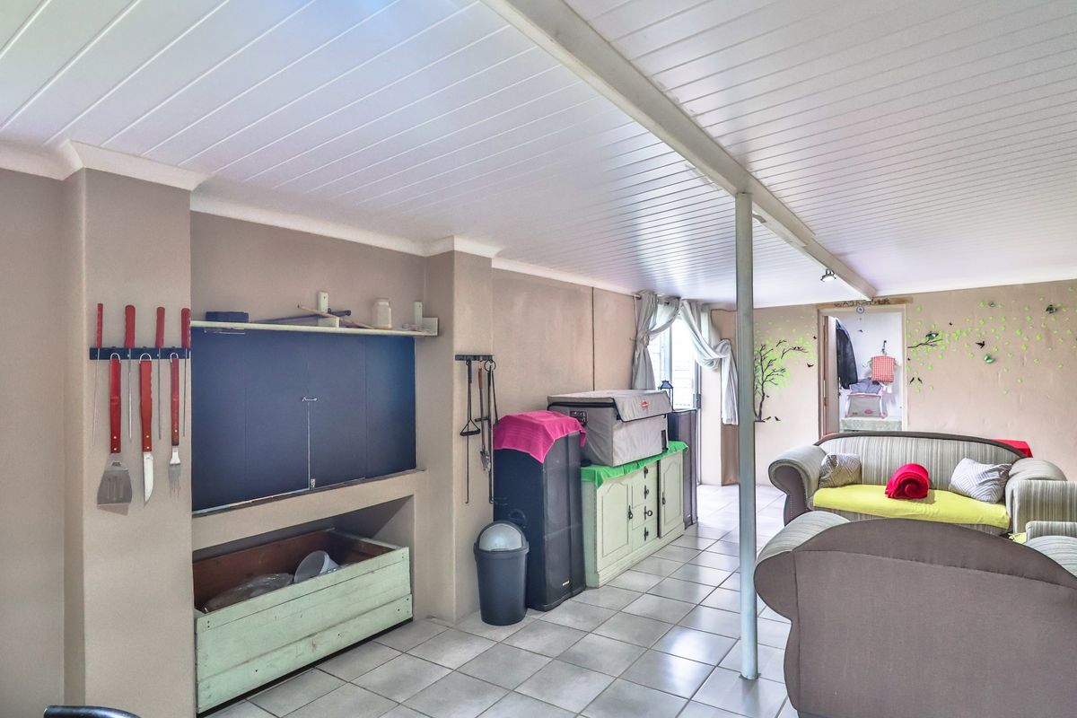 A spacious living area featuring tiled flooring, a built-in fireplace or braai area, and a white panelled ceiling.