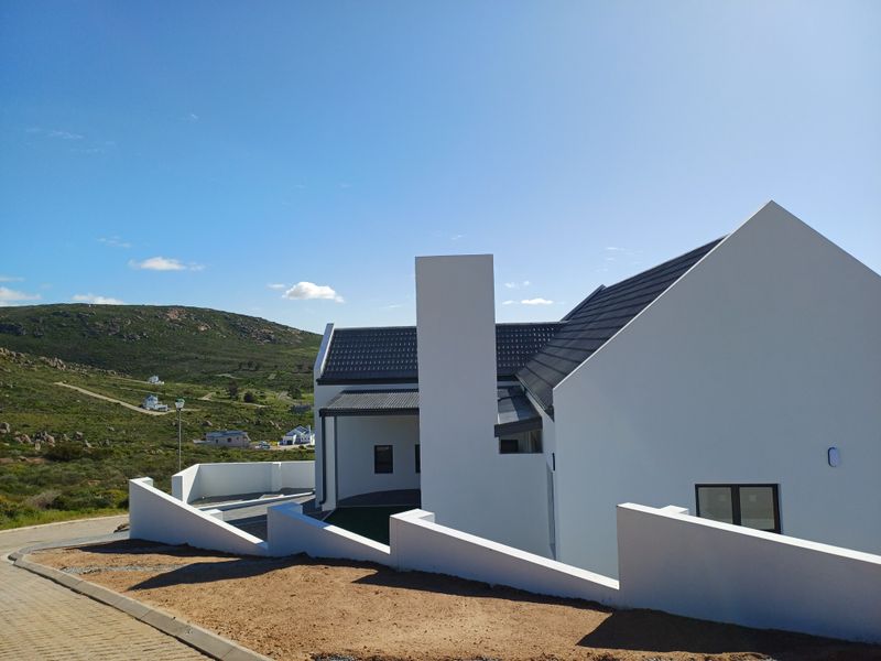 Modern white house exterior with a pitched roof, prominent chimney, and paved driveway, set against a scenic hillside landscape.