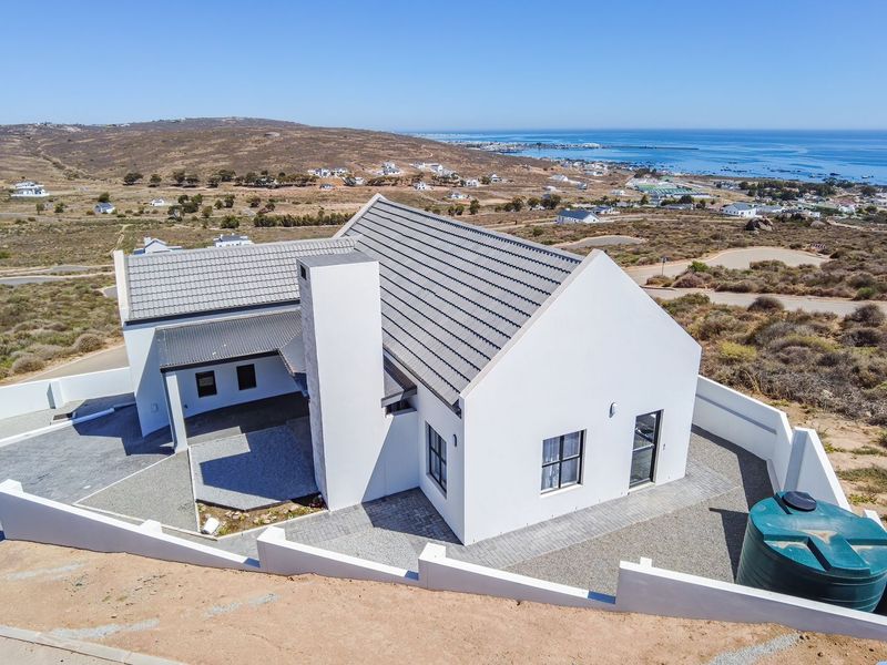 Aerial view of a modern coastal home featuring a tiled roof, prominent chimney, paved exterior areas, and a water tank within a walled perimeter.