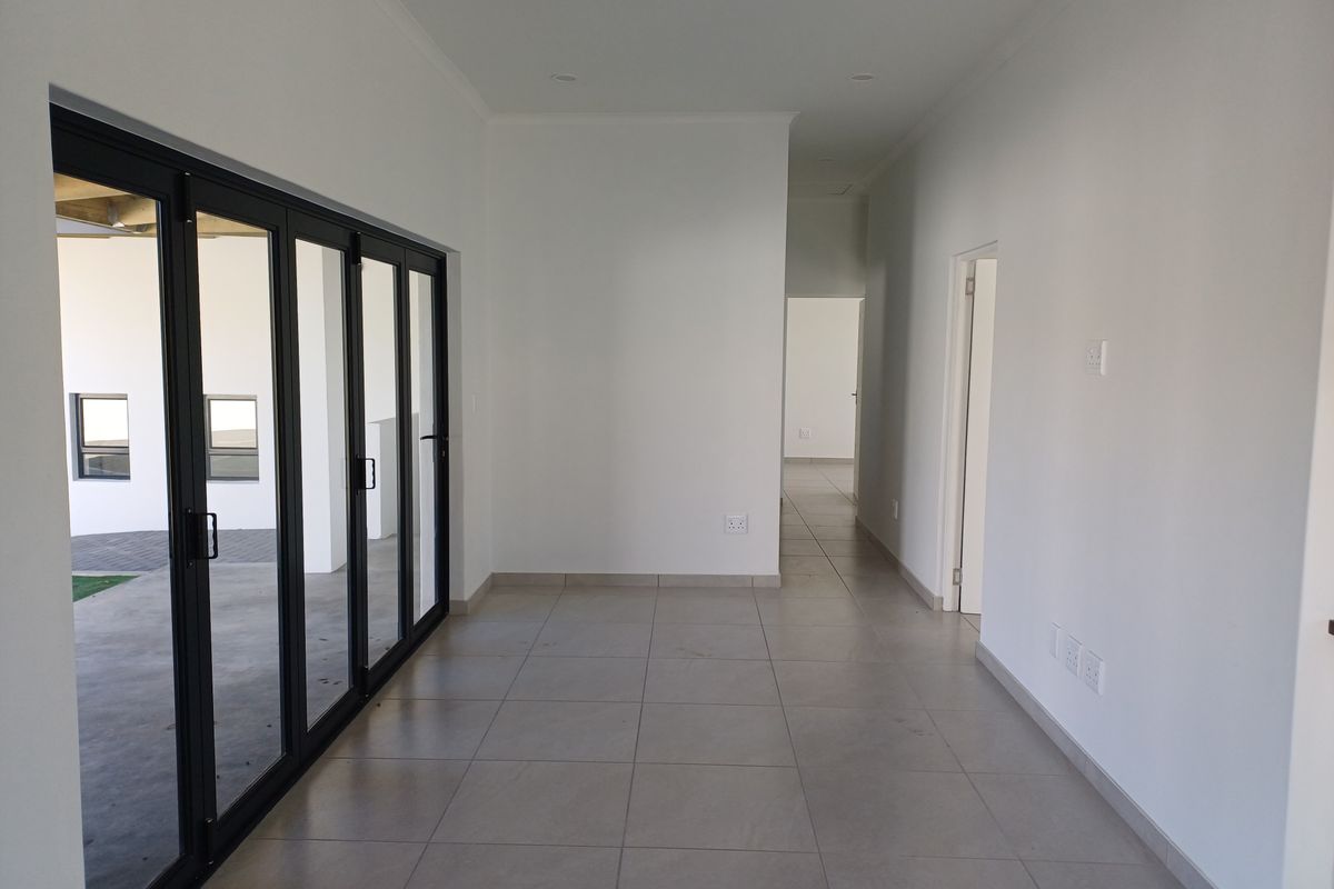 A bright, open-plan living area featuring large black aluminium stacker doors that provide seamless access to the outdoor patio and tiled flooring throughout.