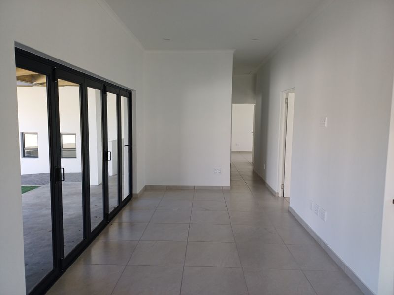 A bright, open-plan living area featuring large black aluminium stacker doors that provide seamless access to the outdoor patio and tiled flooring throughout.