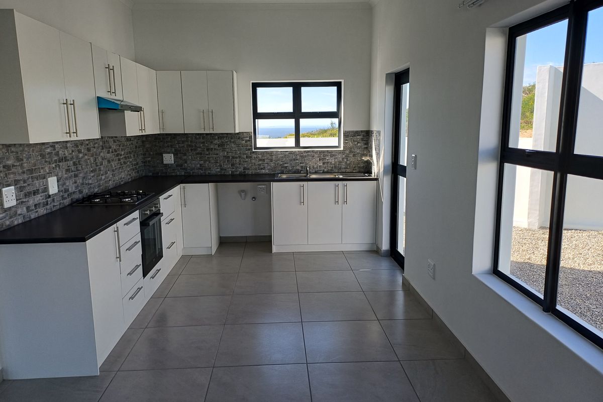 Modern, clean-lined kitchen featuring white cabinetry, dark countertops, gas hob, built-in oven, and tiled flooring with natural light and garden views.