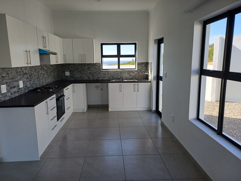 Modern, clean-lined kitchen featuring white cabinetry, dark countertops, gas hob, built-in oven, and tiled flooring with natural light and garden views.