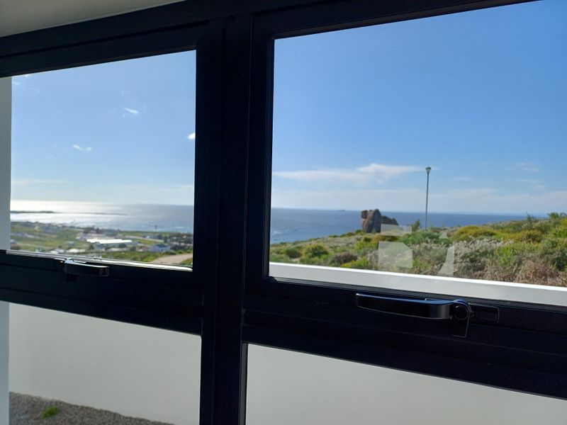 A clear view of the coastline and ocean framed by modern black aluminium casement windows.
