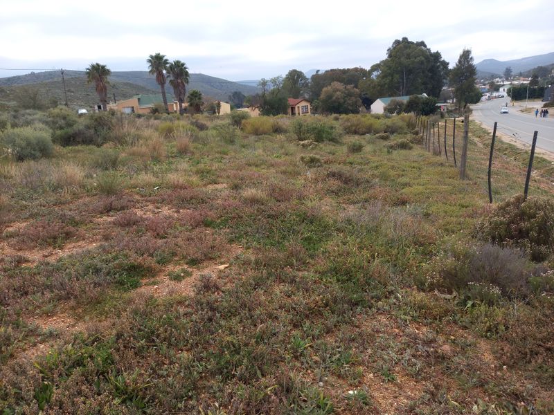 A view of a vacant residential plot featuring natural vegetation and a wire boundary fence, situated adjacent to a public road.