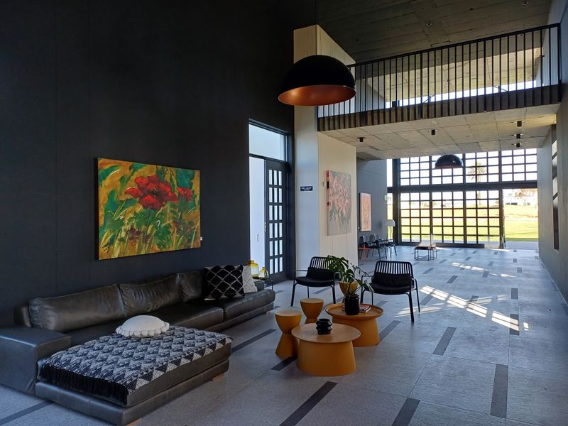 Spacious open-plan area featuring high exposed concrete ceilings, a mezzanine level with metal balustrade, and large grid-pattern glass doors leading to the exterior.