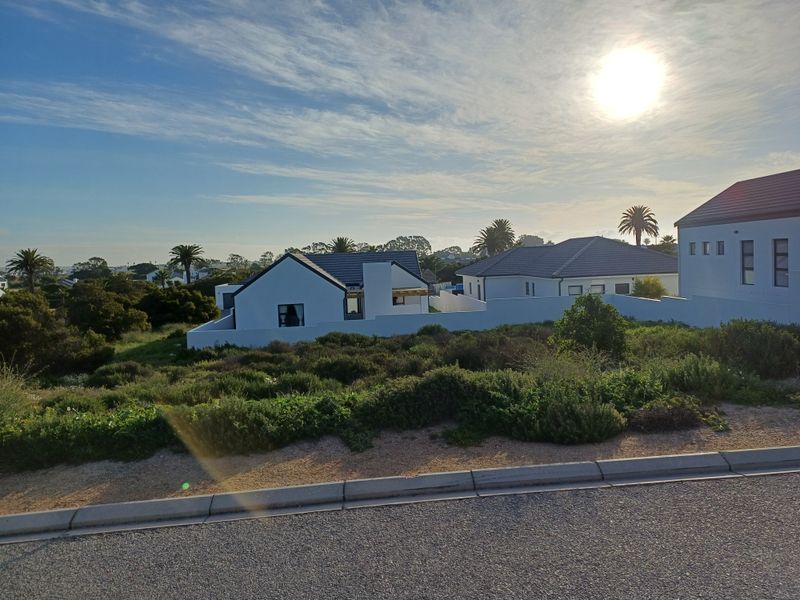 A view of a residential property from the street, featuring white exterior walls, tiled roofing, and surrounding landscaped vegetation.