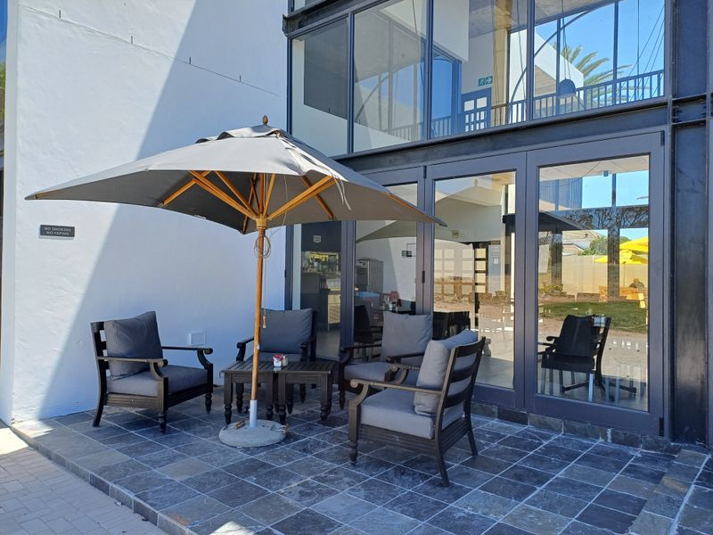 A modern outdoor patio area featuring stone tile flooring and a large glass facade with black metal framing.