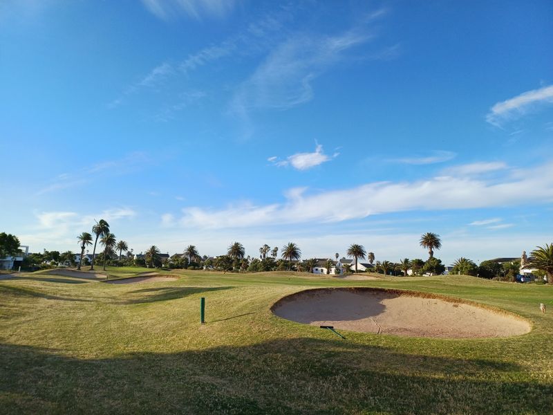 A scenic view of a well-maintained golf course featuring manicured fairways and sand bunkers under a clear blue sky.
