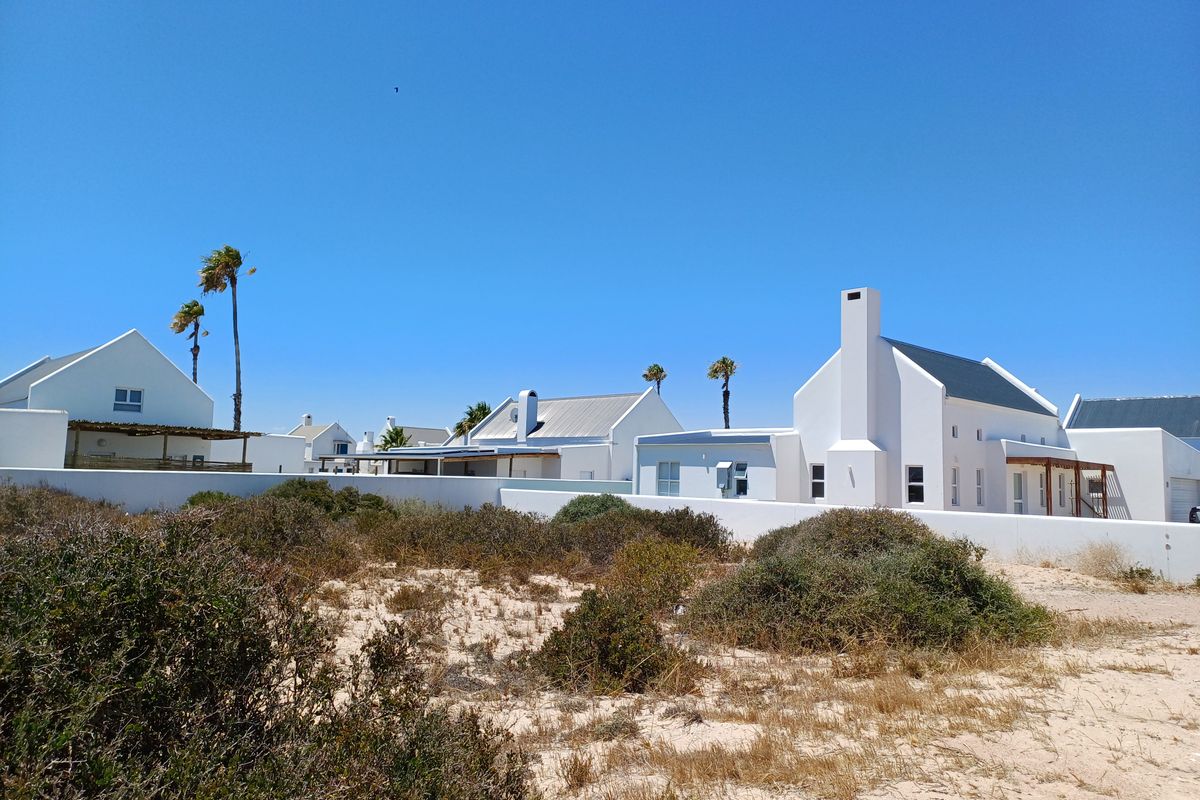 A view of the rear exterior of a white residential property with a chimney, set against a natural coastal landscape.