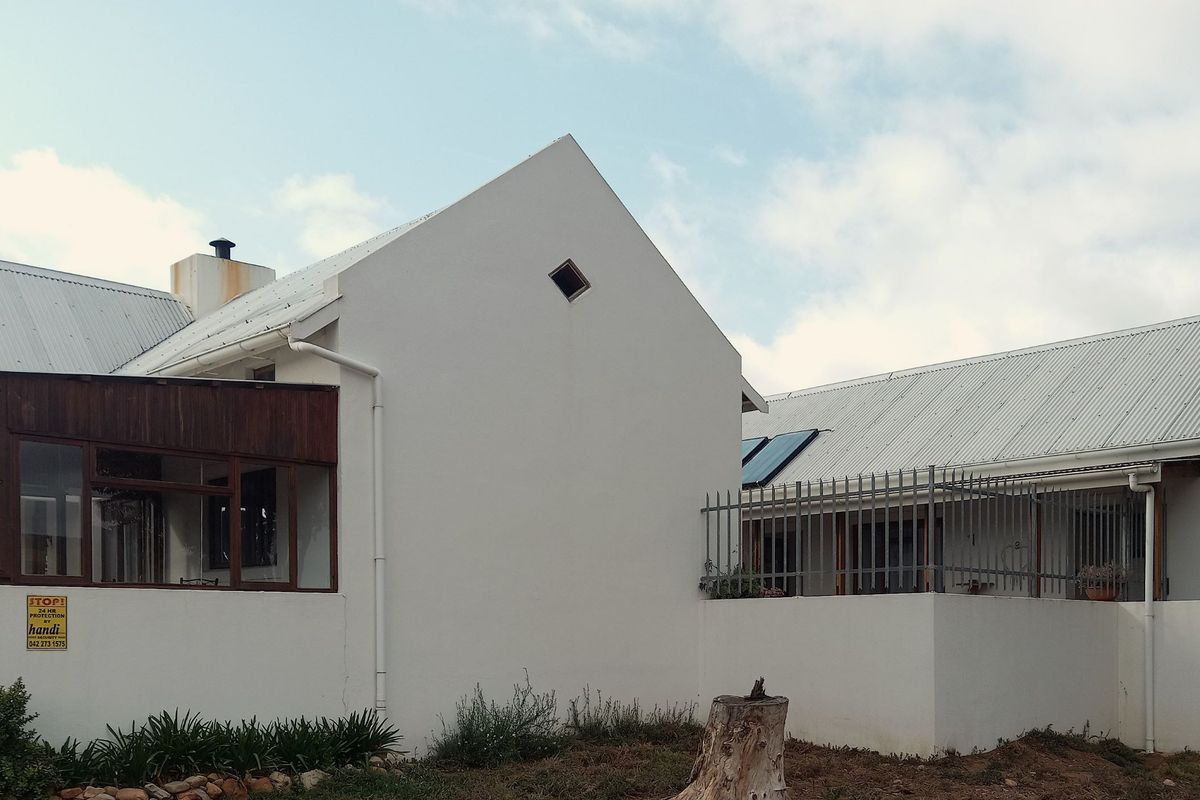 Exterior view of a white house featuring a corrugated metal roof, enclosed patio area, and security fencing.